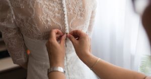 A bride getting her dress adjusted by a family member indoors, highlighting a touching wedding preparation moment.