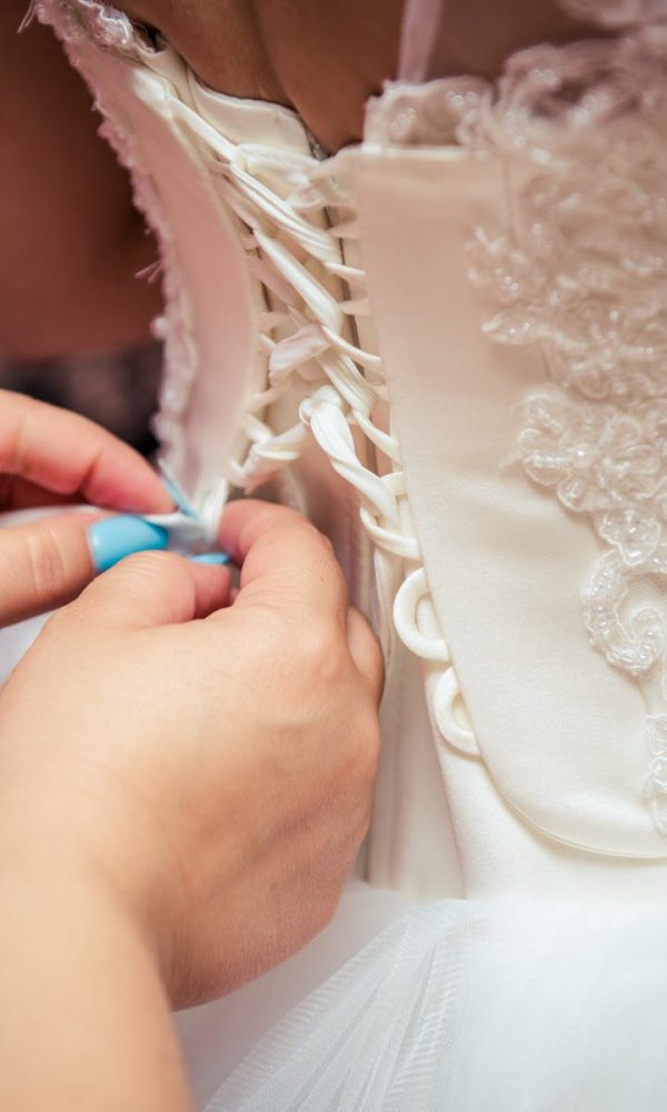 Detailed image of hands lacing a beautiful bridal gown, showcasing elegant wedding preparation.