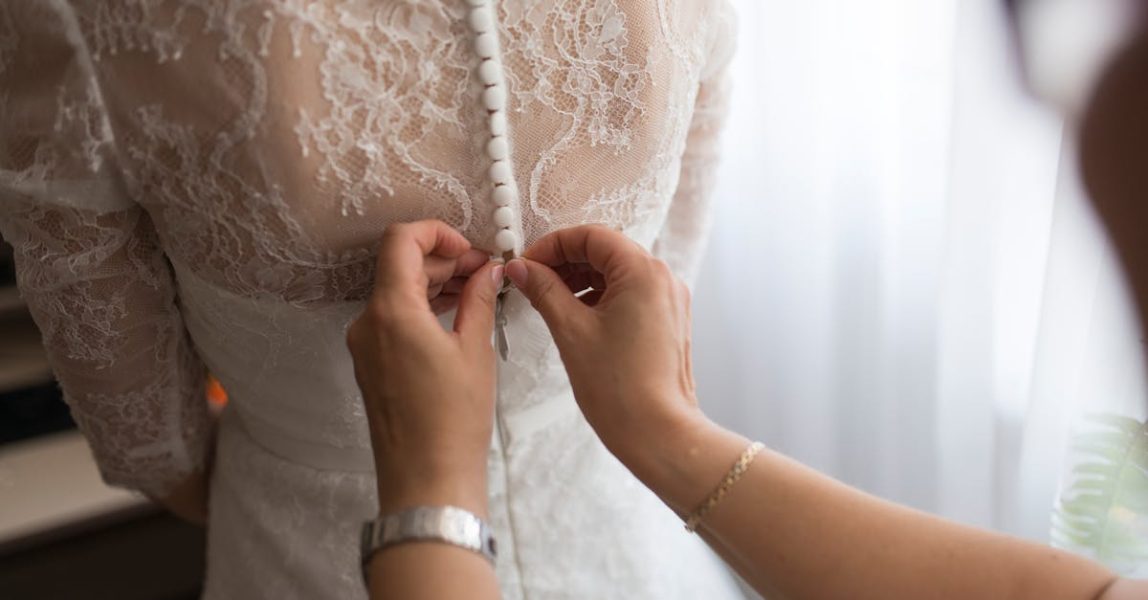 A bride getting her dress adjusted by a family member indoors, highlighting a touching wedding preparation moment.