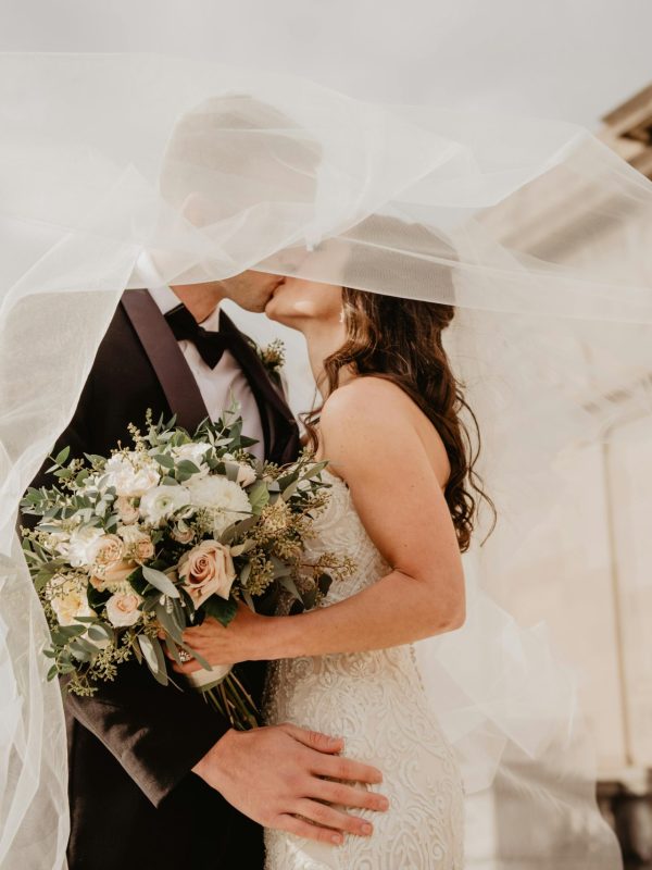 Bride and groom share a tender kiss under a veil, showcasing love and romance on their special day.